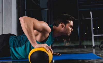 sportsman doing push ups with medicine ball on mat in sports hall